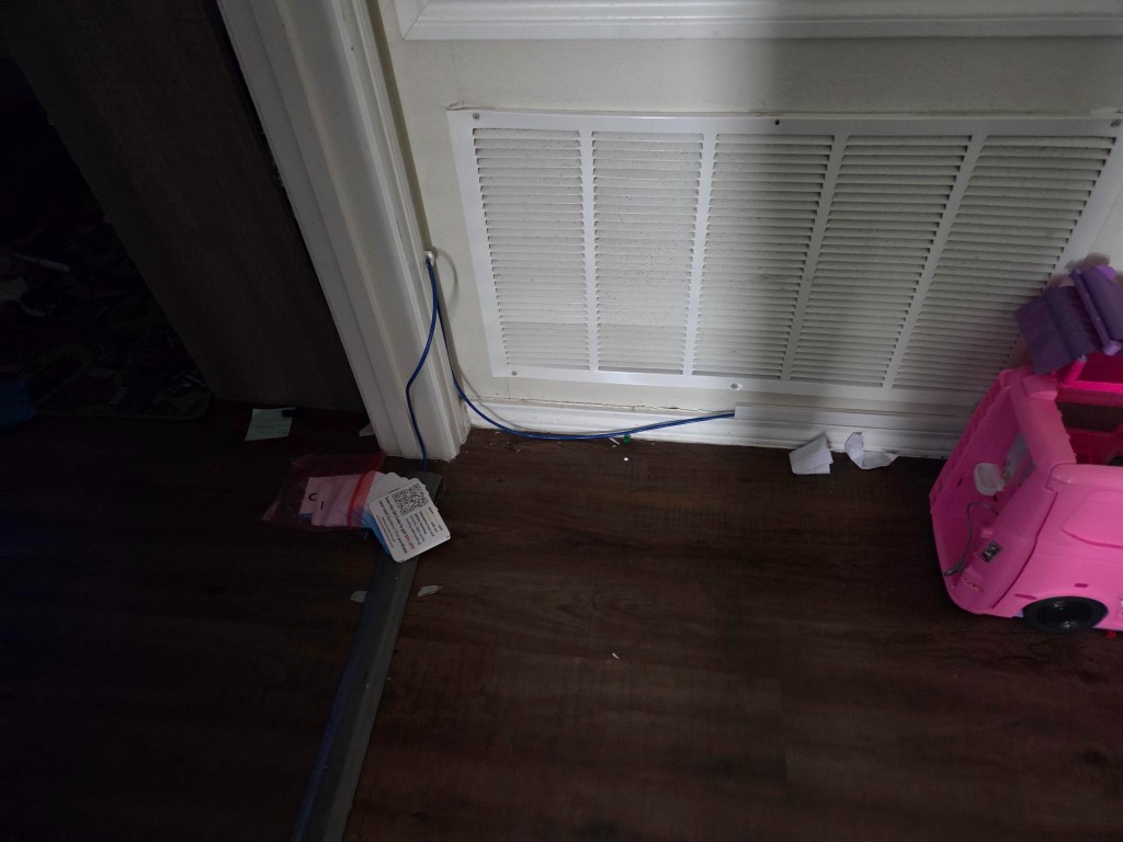Blue ethernet cable running along baseboard under HVAC vent