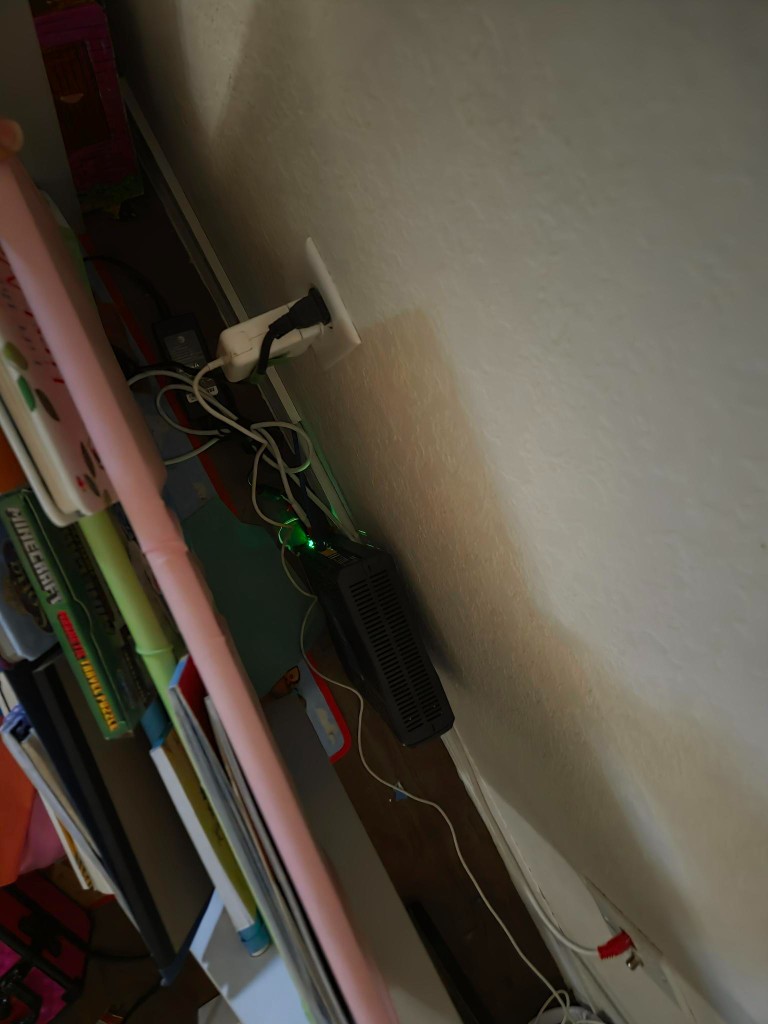 Bridged AT&T router and tangled cables behind a pink kids bookshelf