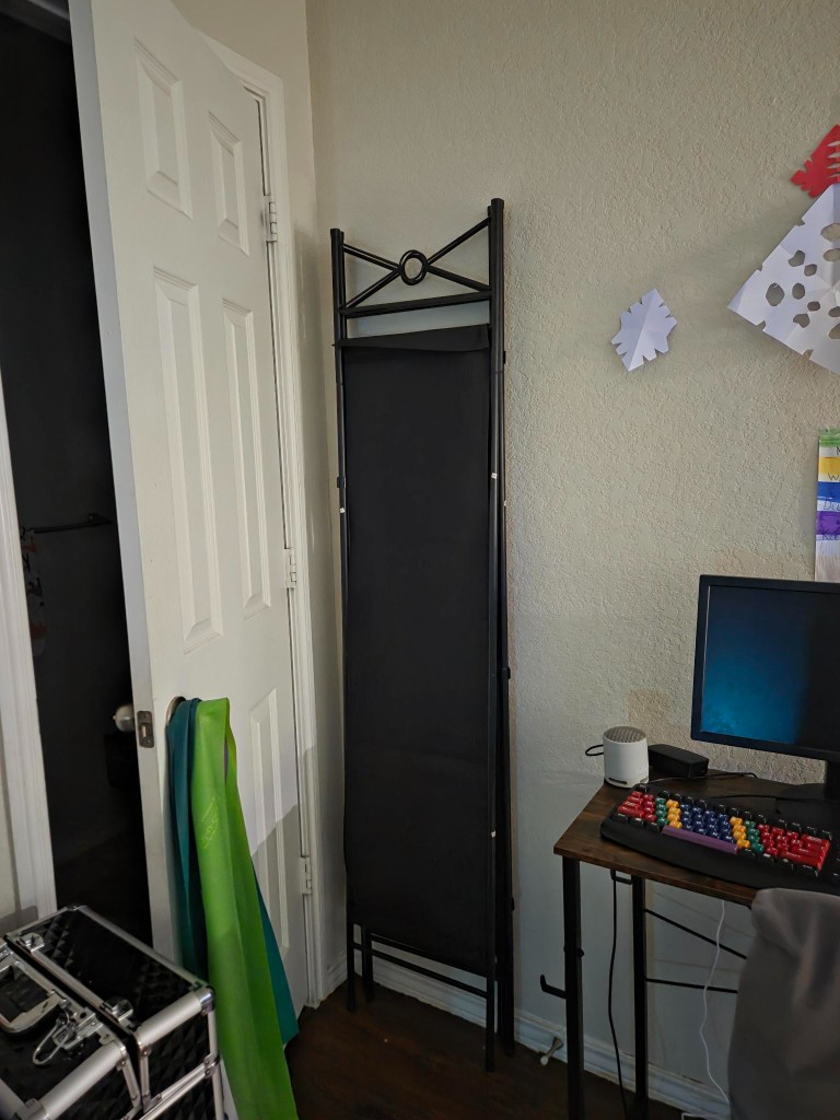 Tall black folding privacy screen leaning near a desk